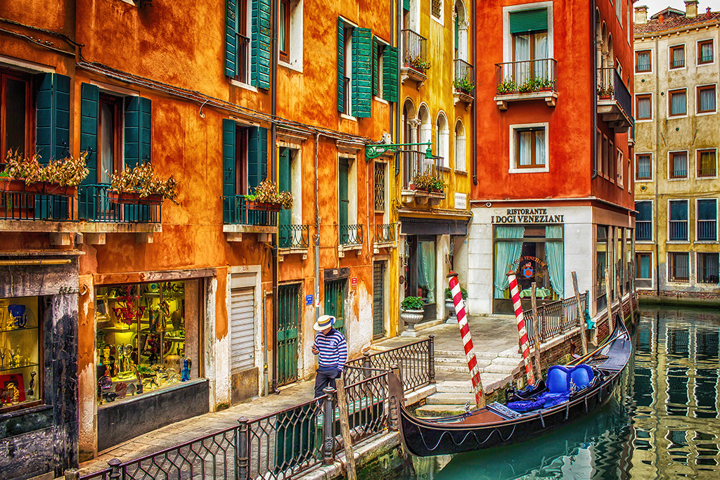 Venetian Dreams: A gondola sits idly on the tranquil canals of Venice, Italy, as the golden hues of sunset cast a warm glow on the historic buildings and the charming Ristorante I Dogi Veneziani. Venice, Italy