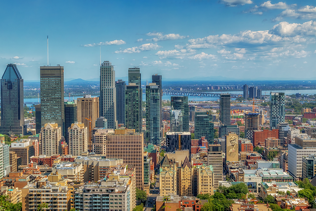 Montreal's Majestic Skyline: Late afternoon view from Mont Royal; a blend of modern skyscrapers and historic architecture is beautifully framed against the backdrop of the St. Lawrence River and the distant Laurentian Mountains.