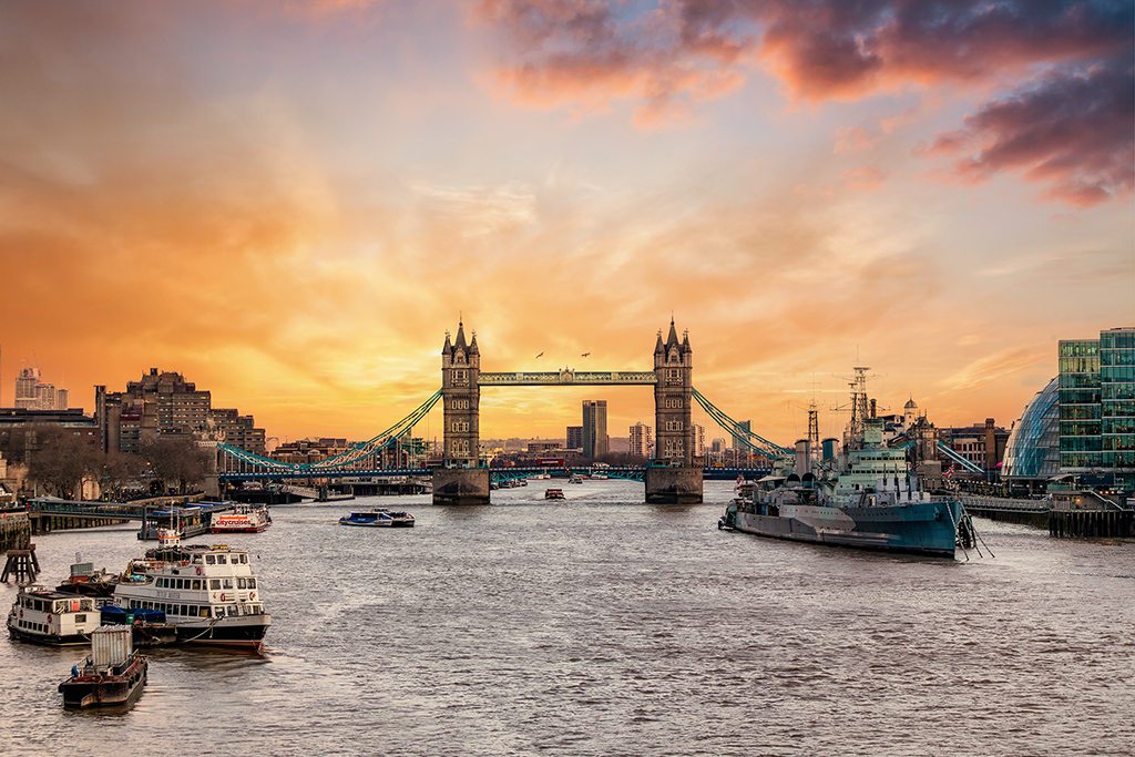 Tower Bridge basking in golden hour grace—Victorian grandeur watching over a city reinvented by glass and steel, mirrored in the timeless flow of the Thames. London, England