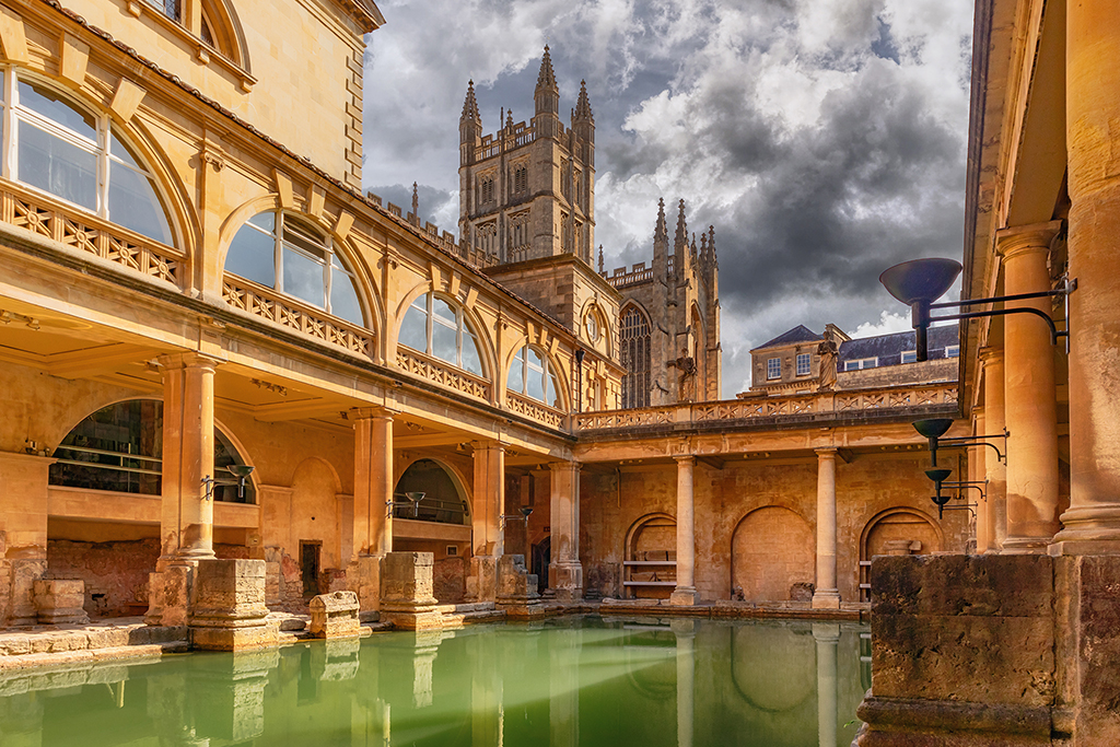 The historic Roman Baths in Bath, England, with the majestic Bath Abbey in the background.