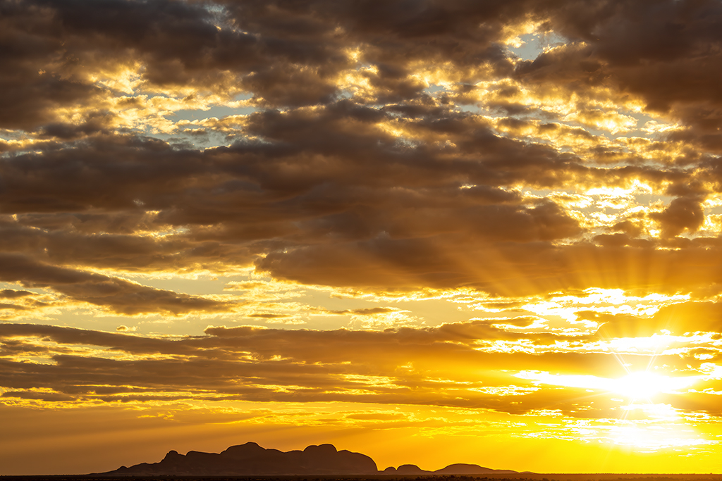 The Olgas silhouetted against a vibrant sunset with golden rays piercing through the clouds. The Red Center, Australia